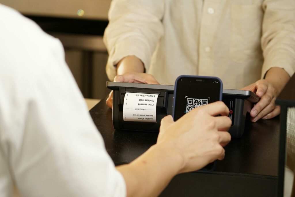 pexels-photo-12935051-12935051 Two individuals engaged in a contactless payment using a QR code scanner at a retail counter.