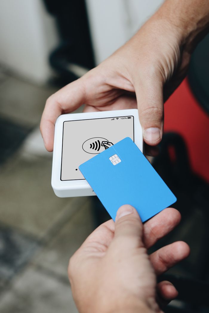Hands using contactless payment terminal and credit card.