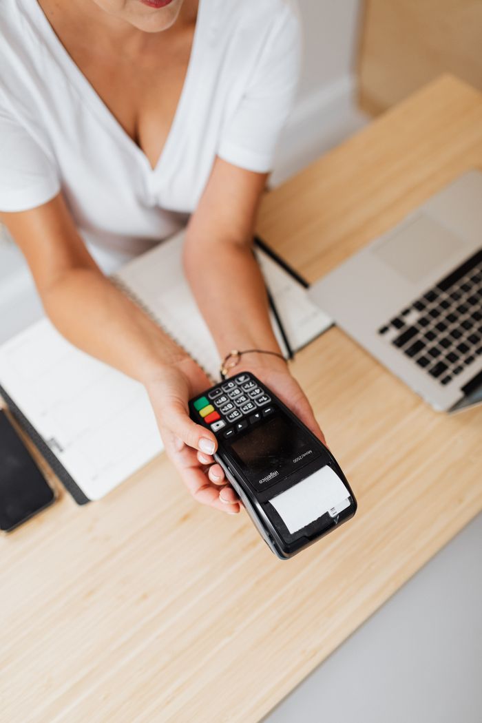 Top view of a woman offering a payment terminal with a receipt on a wooden counter.